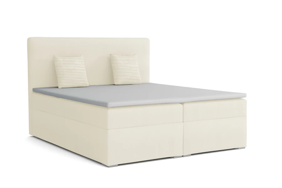 Cremefarbenes Boxspringbett mit grauer Liegefläche und zwei Zierkissen auf weißem Hintergrund.