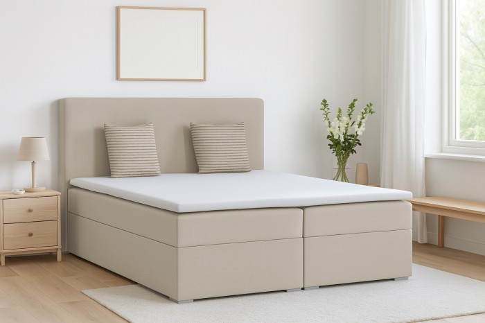 Beiges Boxspringbett in modern eingerichtetem Schlafzimmer mit Kopfteil und Kissen.