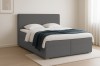 Graues Boxspringbett mit Bouclé-Stoff und blauer Tagesdecke in hellem Schlafzimmer.
