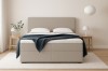 Modernes Bouclé-Boxspringbett in Beige mit hohem Kopfteil und gemütlicher blauer Decke.