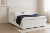 Elegantes weißes Boxspringbett aus Bouclé-Stoff mit dunkler Decke in hellem Ambiente.