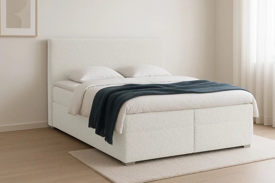 Elegantes weißes Boxspringbett aus Bouclé-Stoff mit dunkler Decke in hellem Ambiente.
