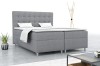 Graues Boxspringbett in modern eingerichtetem Schlafzimmer mit Beistelltisch und Zimmerpflanze.