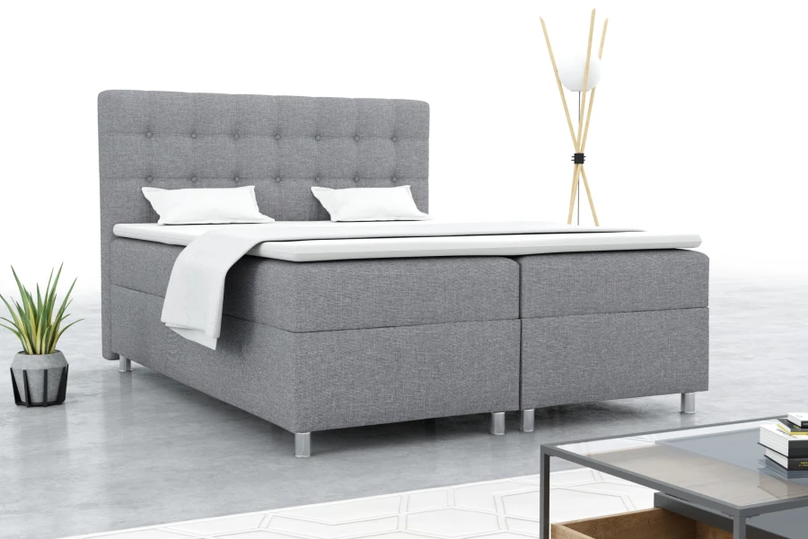 Graues Boxspringbett in modern eingerichtetem Schlafzimmer mit Beistelltisch und Zimmerpflanze.