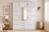 Modern white wardrobe with mirror and many drawers in a bright bedroom.