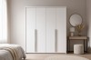 Schlichter weißer Kleiderschrank 4-türig in hellem Schlafzimmer mit Schminktisch und Spiegel.