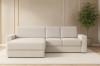 Cremefarbenes L-Sofa im Wohnzimmer mit Pflanze und hellem Teppich.