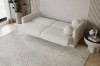 Perspektivische Ansicht eines beigen Bouclé-Sofas auf einem gemusterten Teppich.
