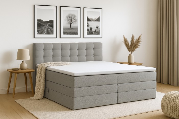 Hellgraues Boxspringbett mit gestepptem Kopfteil in hell eingerichteter Schlafzimmer-Umgebung.