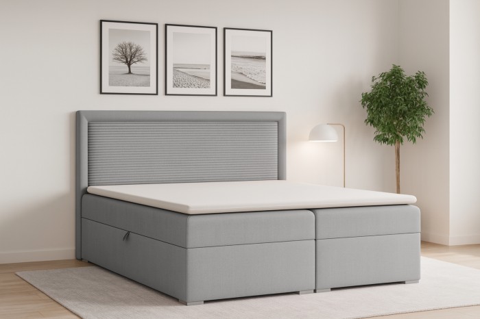 Hellgraues Boxspringbett John II im Schlafzimmer-Ambiente mit Wanddeko und Pflanze.