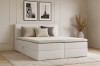 Modernes weißes Boxspringbett in hellem Schlafzimmer mit Kissen und Teppich.