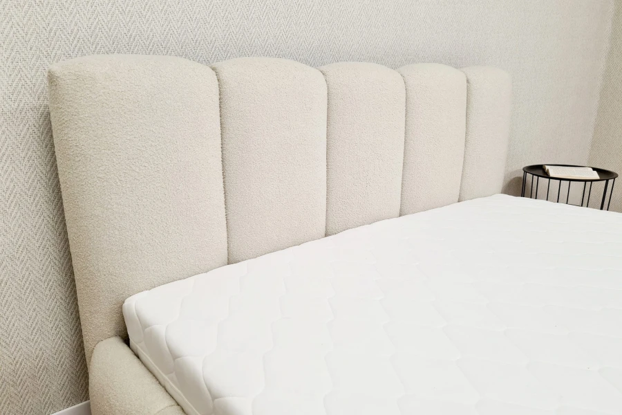 Gepolstertes Kopfteil aus beigem Bouclé-Stoff mit vertikaler Steppung für ein modernes Schlafzimmer.