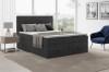 Modernes Schlafzimmer-Design mit grauem Boxspringbett, Teppich und blauem Sessel.