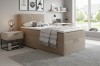Gemütliches Schlafzimmer mit beigem Boxspringbett, Nachttisch und grauem Teppich.