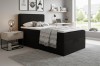 Gemütliches Schlafzimmer mit modernem schwarzem Boxspringbett, Teppich und hellem Ambiente.