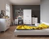 Modernes Schlafzimmer mit weißen Möbeln, Kleiderschrank, Schreibtisch und gelber Bettwäsche.
