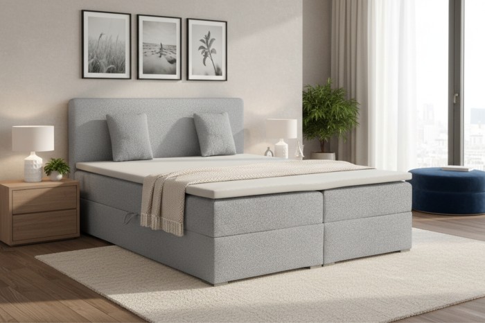 Modernes graues Boxspringbett im hellen Schlafzimmer mit zwei Kissen und Decke.