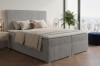 Hellgraues Boxspringbett mit Cord-Bezug in modernem Design vor einer beeindruckenden Skyline.