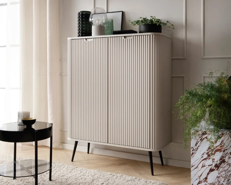 Modernes beiges Highboard mit Rillenstruktur und schwarzen Beinen in wohnlicher Umgebung.