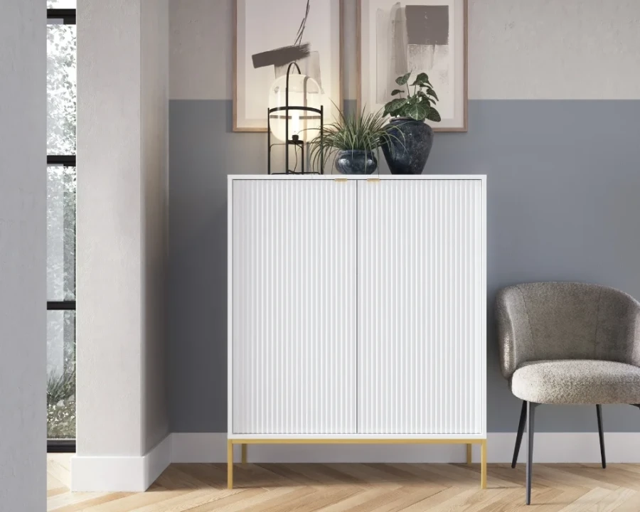 Weißes Highboard mit Rillenfront dekorativ platziert neben einem Sessel.