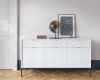 Stilvoll dekoriertes weißes Sideboard mit Rillenfront im hellen Wohnzimmer vor weißer Wand.