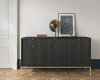 Stilvoll dekoriertes schwarzes Sideboard mit goldenen Füßen vor einer hellen Wand im Wohnbereich.