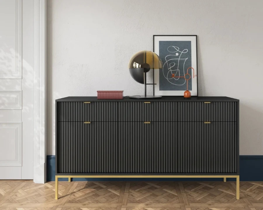 Stilvoll dekoriertes schwarzes Sideboard mit goldenen Füßen vor einer hellen Wand im Wohnbereich.