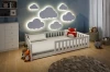Weißes Kinderbett mit Rausfallschutz in gemütlichem Kinderzimmer mit leuchtenden Wolkenlampen.