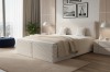 Helles Boxspringbett in Creme mit gerippter Textur in einem lichtdurchfluteten Schlafzimmer.