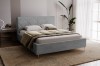 Grijs gestoffeerd bed in een modern ingerichte slaapkamer met tapijt en plant.