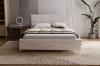 Licht gestoffeerd bed in beige met gecapitonneerd hoofdbord en gouden poten op tapijt.