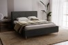 Elegantes dunkelgraues Bett in modernem Schlafzimmer mit Teppich und Pflanze für gemütliches Ambiente.