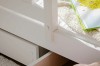 Detailaufnahme eines weißen Bettrahmens aus Holz mit einer ausziehbaren Schublade.