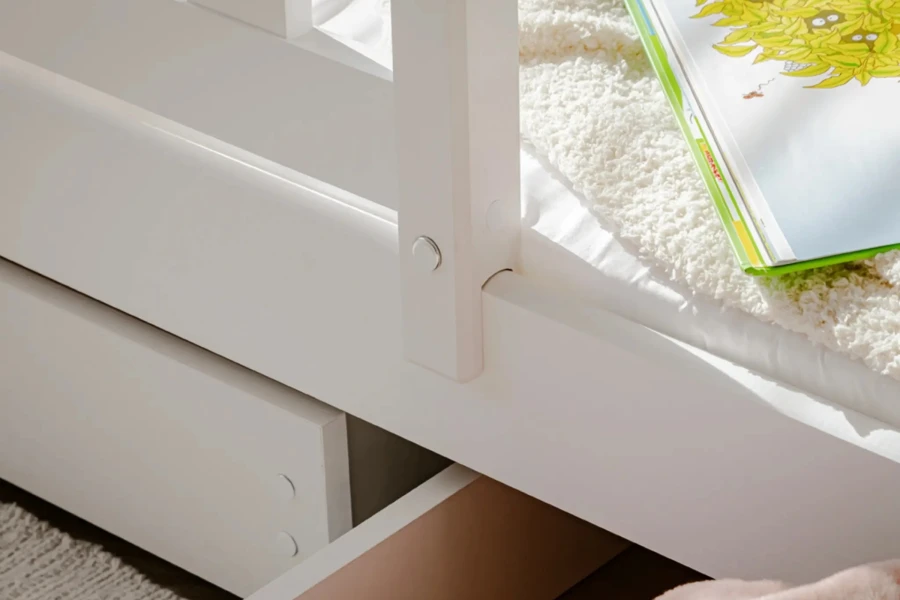 Detailaufnahme eines weißen Bettrahmens aus Holz mit einer ausziehbaren Schublade.